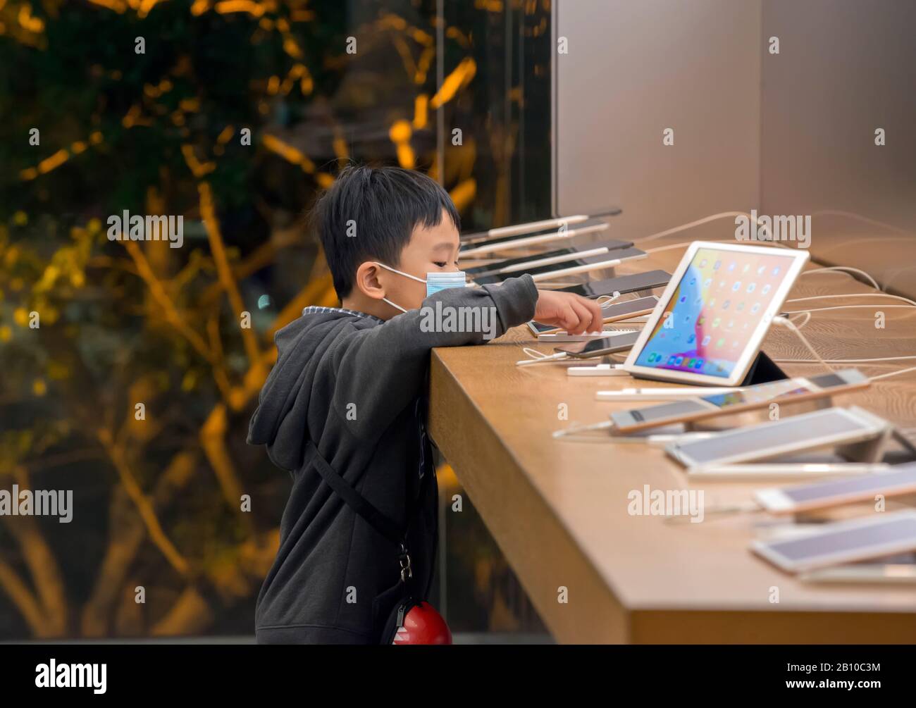 Giovane ragazzo cinese in un negozio di computer che gioca con computer portatili e smartphone, Hong Kong, Cina. Foto Stock
