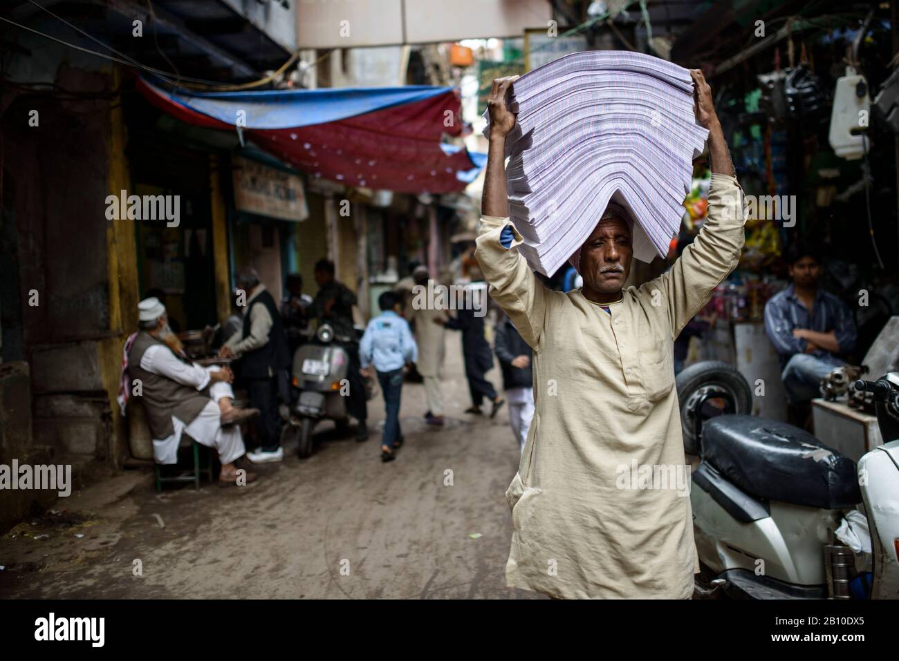 L'uomo trasporta mucchi di carta attraverso le strade della vecchia Delhi, India Foto Stock