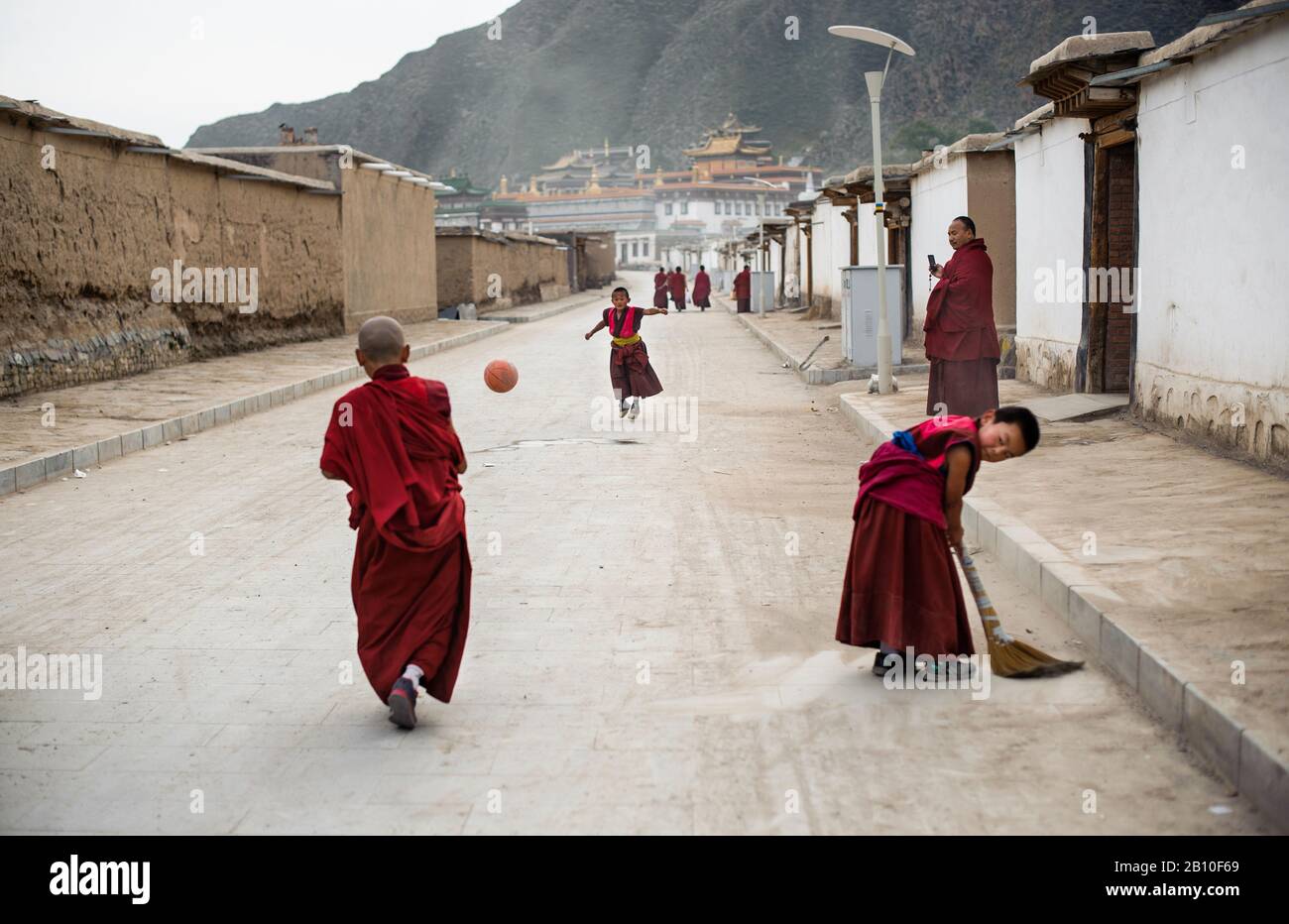 I piccoli monaci giocano a calcio per le strade del villaggio del Monastero di Labrang, provincia di Gansu, Cina Foto Stock