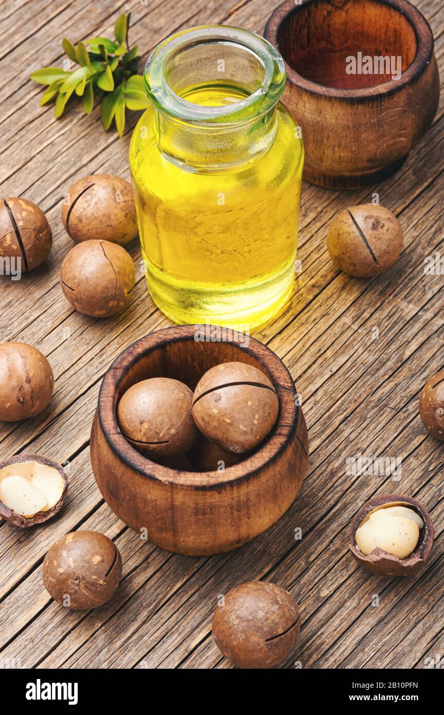 Olio di noce macadamia e noce macadamia su fondo di legno.bottiglie di vetro con olio di macadamia Foto Stock