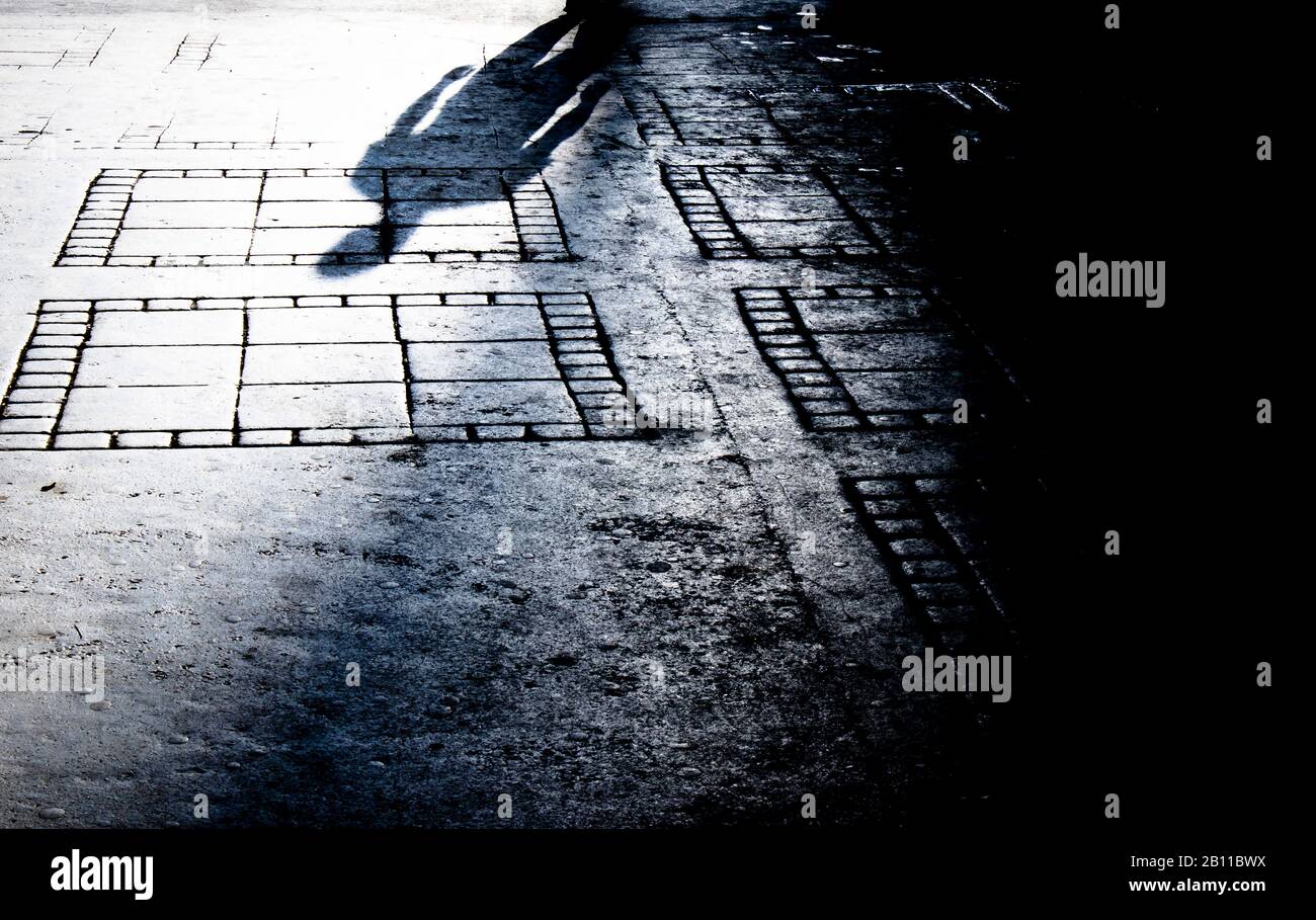 Silhouette sfumata di un uomo che cammina da solo la notte sul marciapiede della strada della città in bianco e nero Foto Stock