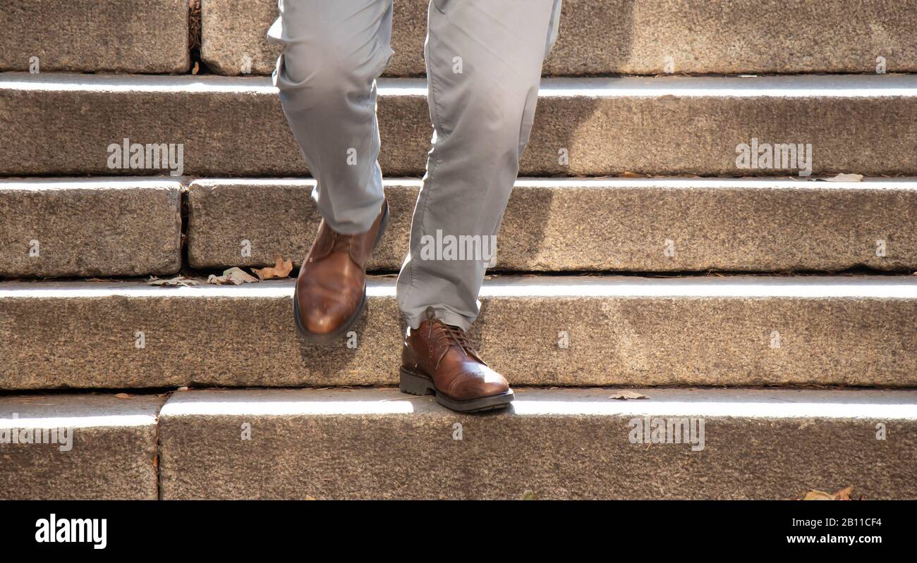 Un uomo con scarpe marroni che cammina lungo la scala pubblica all'aperto in autunno luce del sole, dettaglio delle sue gambe in movimento sfocatura Foto Stock
