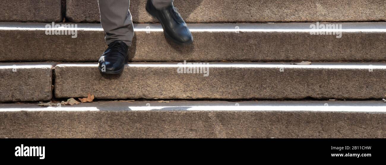 Un uomo con scarpe nere che cammina lungo la scala pubblica all'aperto, dettaglio dei suoi piedi in movimento sfocato Foto Stock