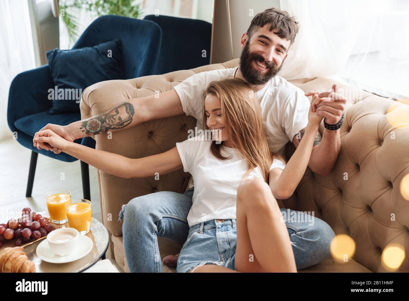 Immagine della romantica coppia compiaciuta che rende divertente e avvolgente mentre si fa colazione in sala luminosa a casa Foto Stock