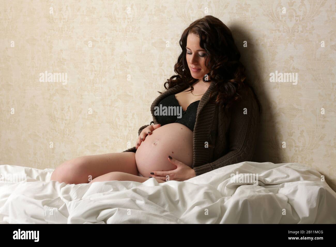 Una donna incinta è seduta sul letto Foto Stock