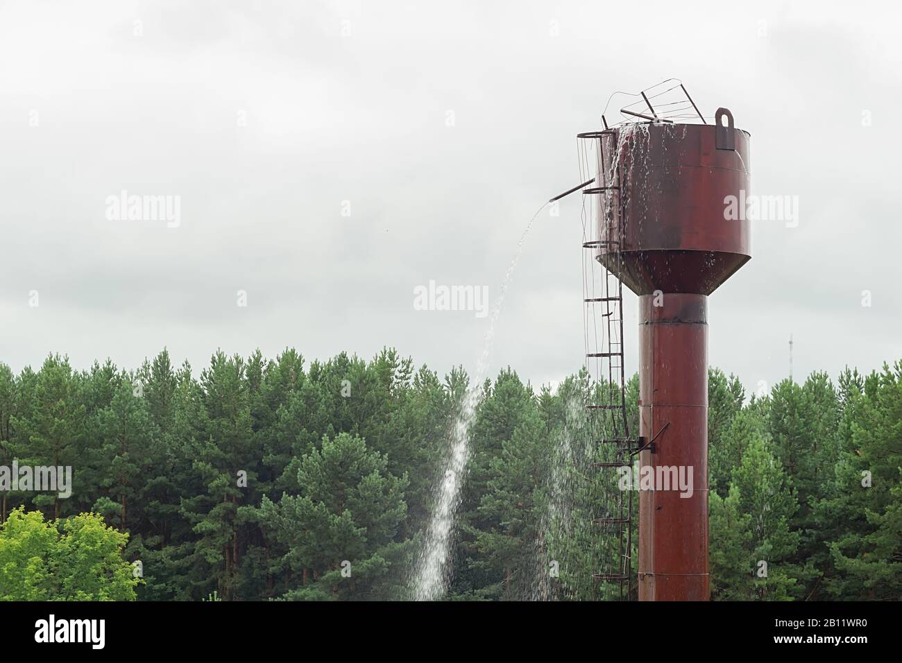 vista di un villaggio difettoso vecchia torre di acqua di metallo, da cui l'acqua è versata Foto Stock
