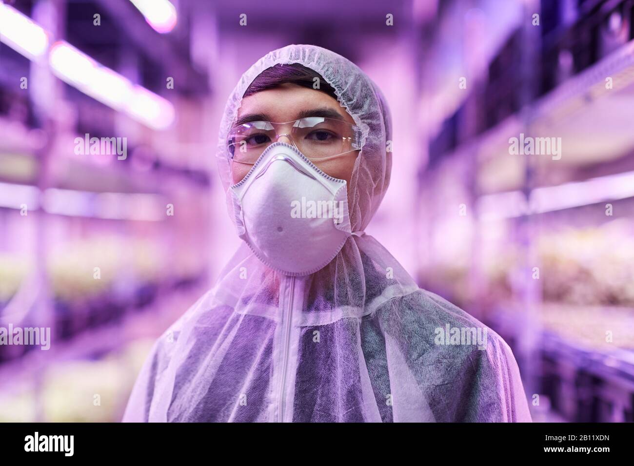 Ritratto di chimico asiatico in indumenti da lavoro protettivi e maschera protettiva guardando la macchina fotografica Foto Stock