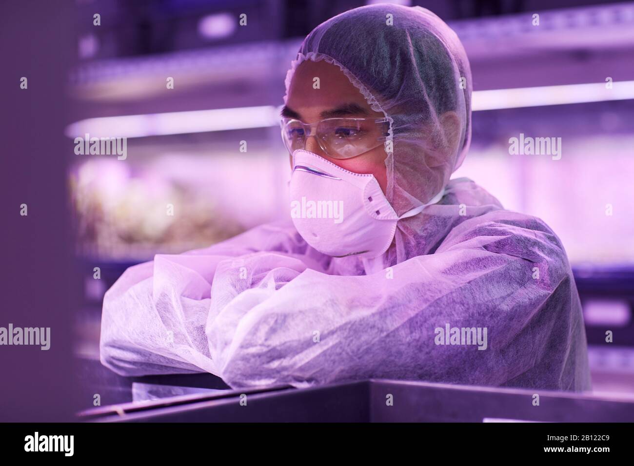 Scienziato asiatico in abbigliamento protettivo e maschera protettiva che lavora con i prodotti chimici Foto Stock