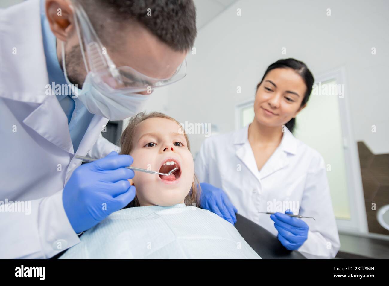 Giovane dentista che usa lo specchio dentale durante l'esame orale della bambina Foto Stock