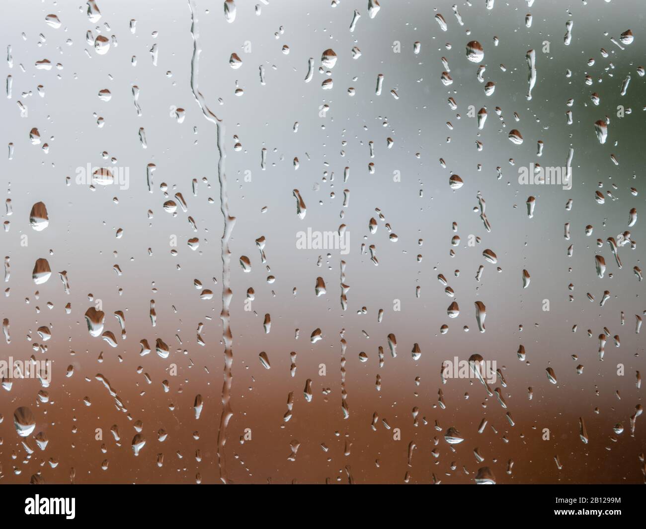 Gocce di pioggia sulla superficie del vetro del finestrino con sfondo nuvoloso . Modello naturale di gocce di pioggia isolato su sfondo sfocato. Foto Stock