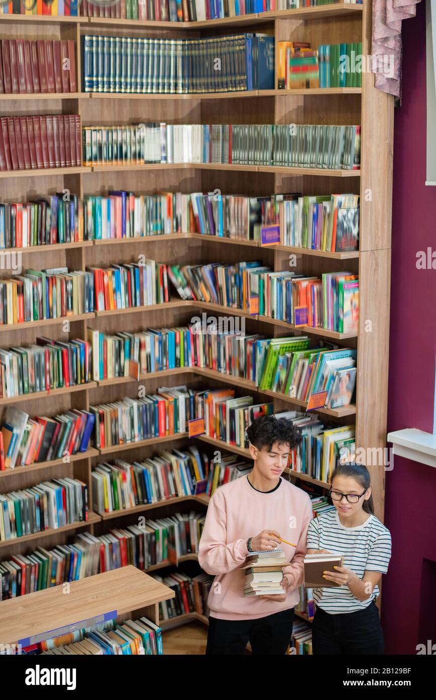 Ragazzo intelligente adolescente che punta alla copertina del libro tenuto dal suo compagno di classe Foto Stock