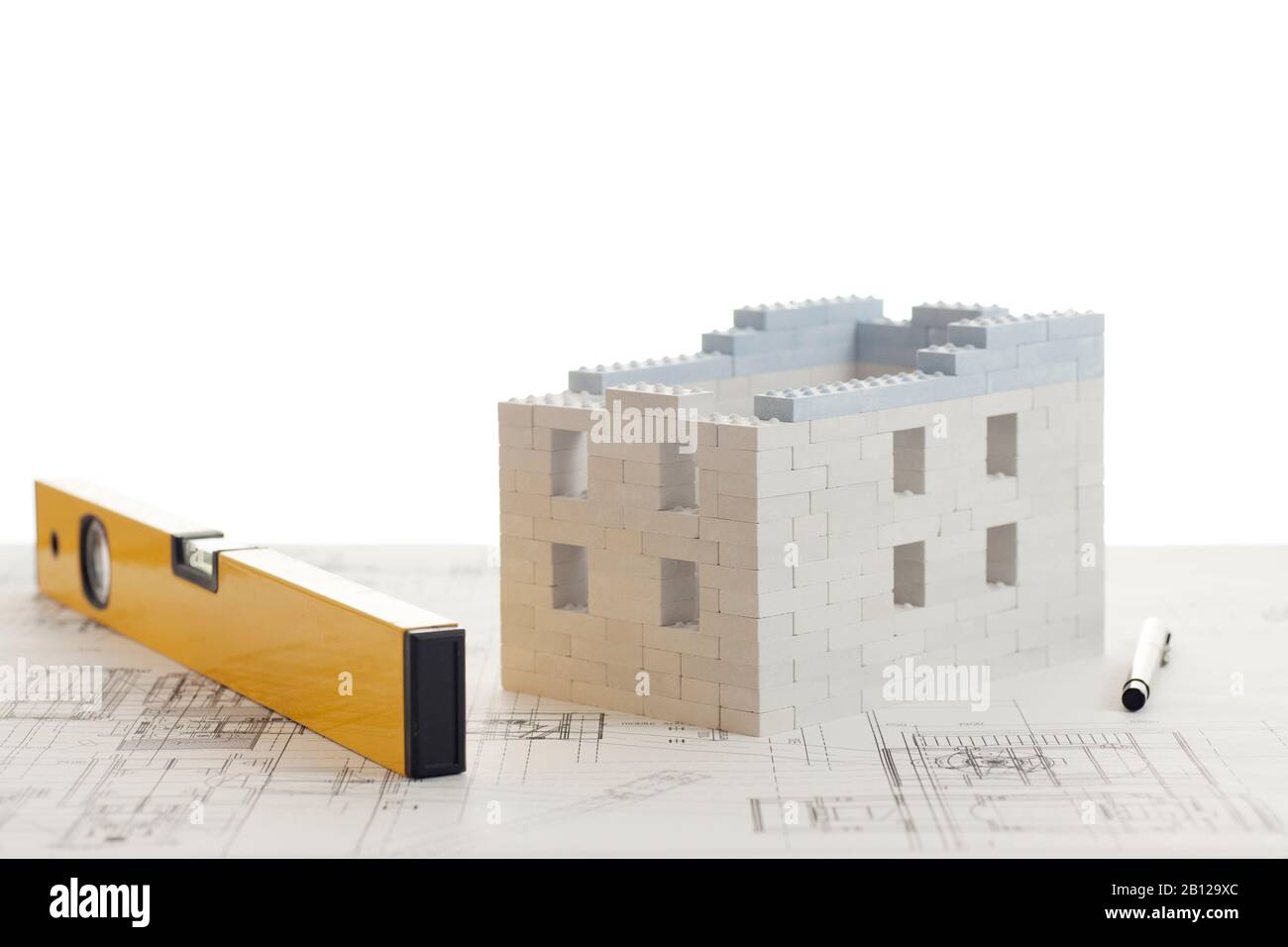 Casa di blocchi giocattolo con calcolatrice e penna su piano di costruzione - sfondo bianco Foto Stock