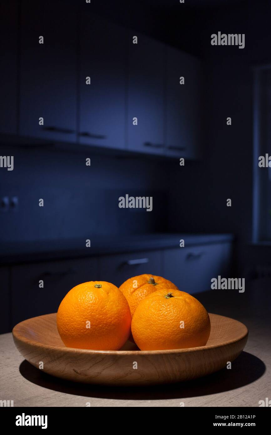 Tre arance in una ciotola di frutta di legno in una cucina presto al mattino o di notte Foto Stock