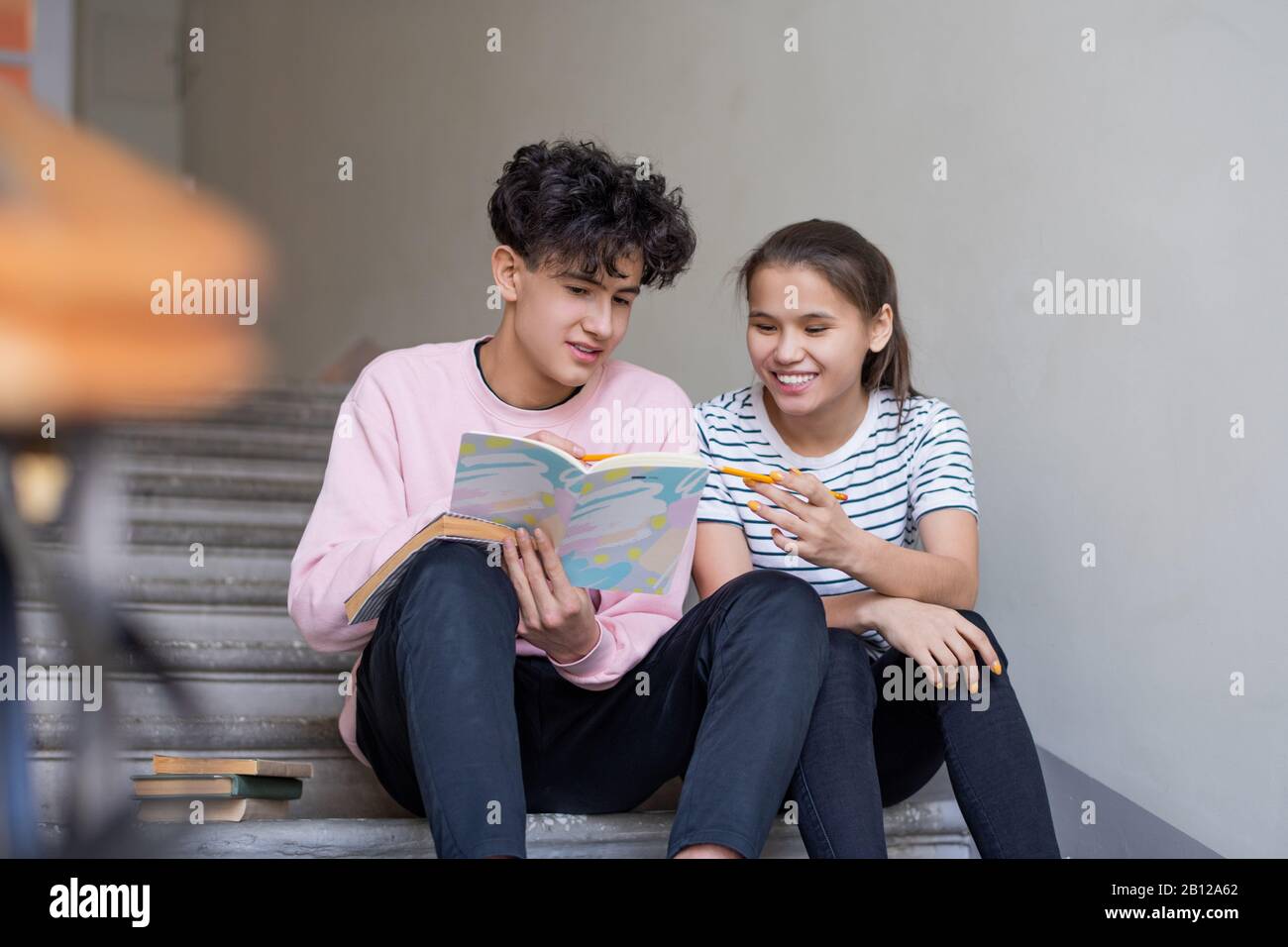 Ragazzo e ragazza intelligente che punta alla pagina del copybook mentre discute le note della lezione Foto Stock