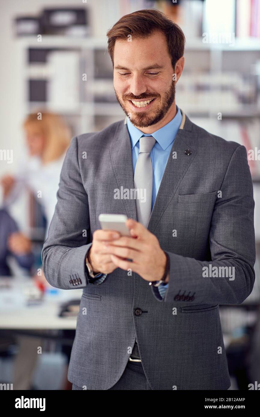 Un uomo d'affari sorridente al lavoro scrive un messaggio su un telefono mobile. Foto Stock