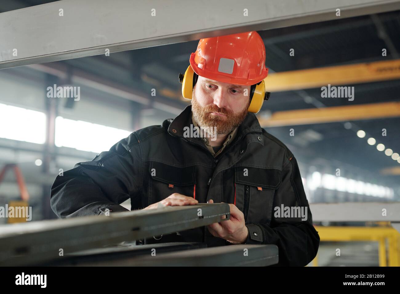 Giovane ingegnere bearded in casco protettivo e dettagli di elaborazione cuffie Foto Stock