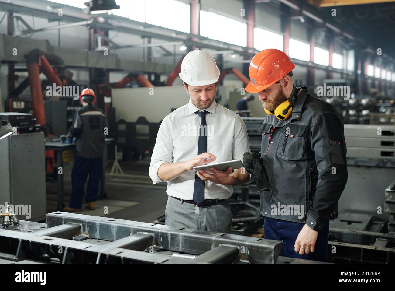 Giovane maestro in hardhat e tecnico bearded che discute lo schizzo tecnico Foto Stock