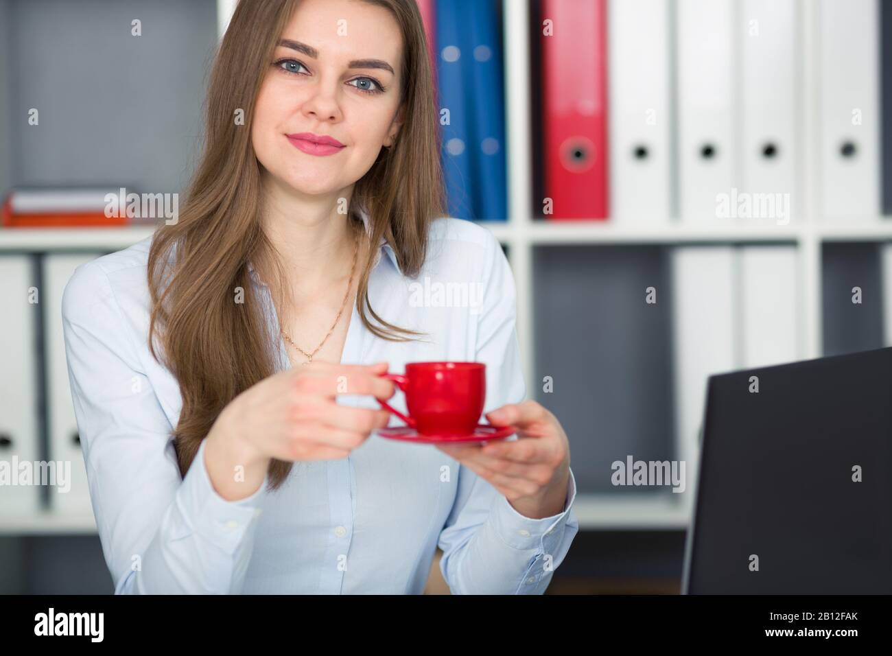 Donna d'affari che tiene una tazza rossa di caffè nelle sue mani. Pausa sul lavoro. Guarda la fotocamera. Foto Stock