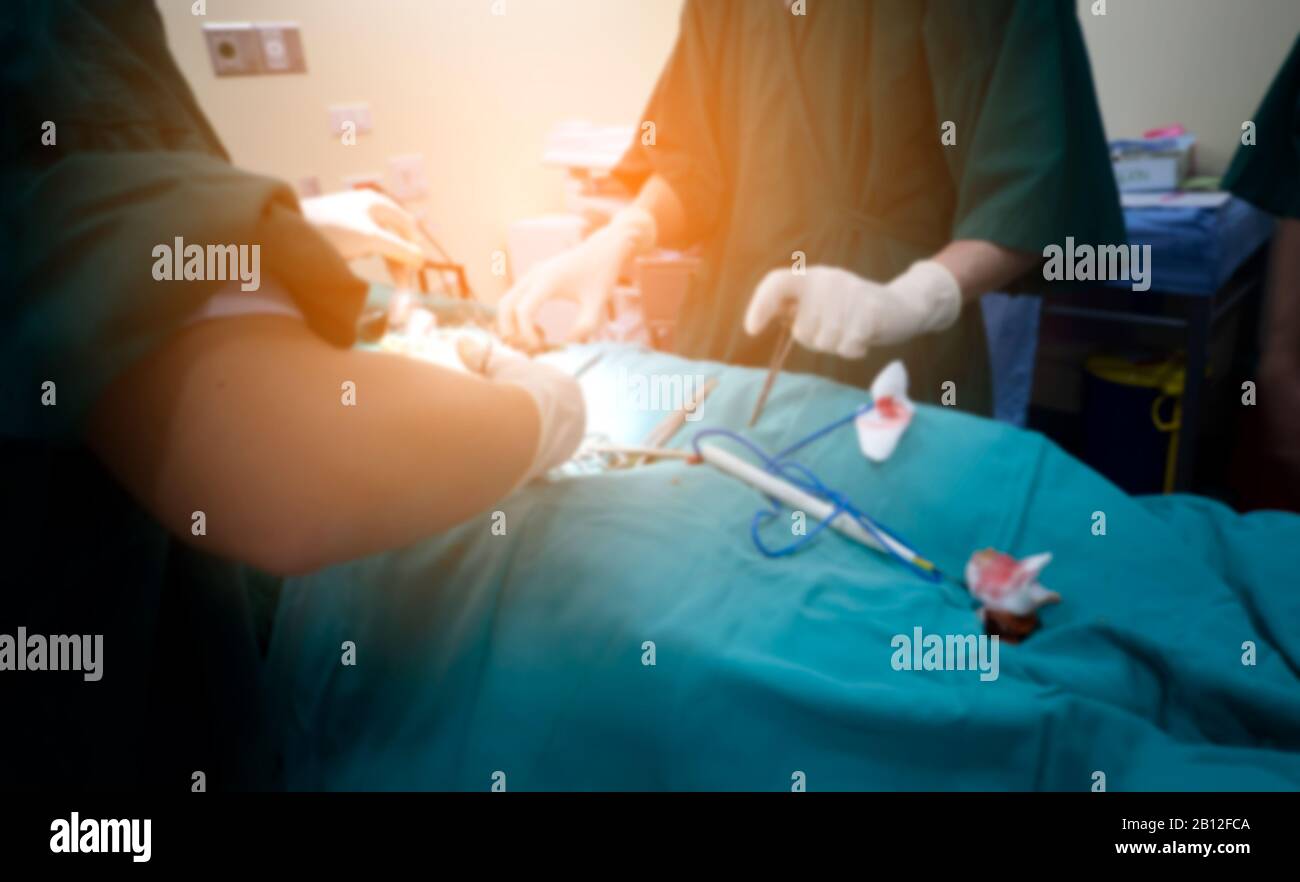 Immagine offuscata del team di chirurghi che eseguono interventi chirurgici in ambiente sterile ospedaliero o del gruppo di chirurghi nella sala operatoria con apparecchiature chirurgiche. Foto Stock