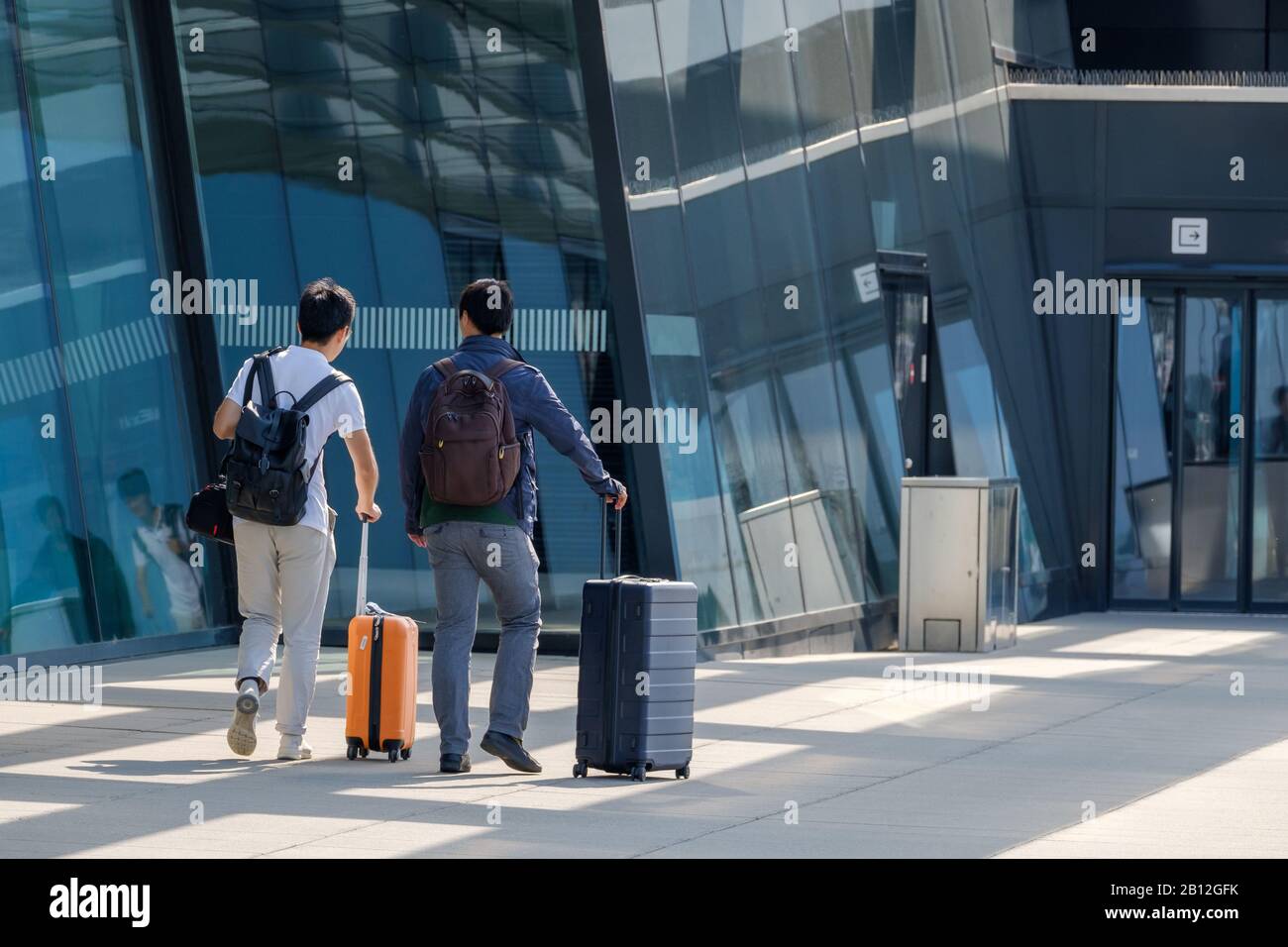 Due viaggiatori vanno all'ingresso dell'aeroporto con valigie Foto Stock