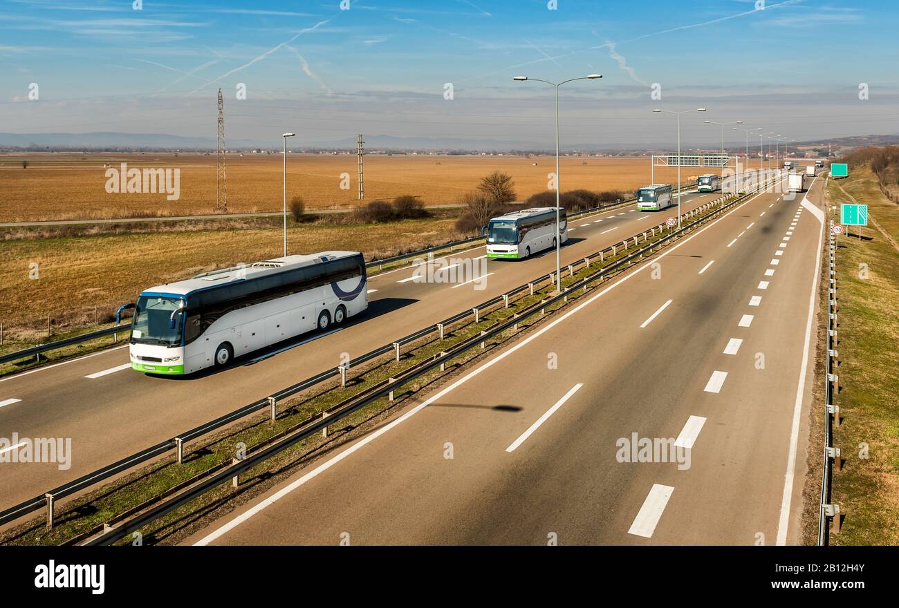 Caravan o convoglio di Quattro autobus bianchi in linea che viaggiano su un'autostrada di campagna sotto il cielo blu stupefacente. Highway scuola bambini trasporto con bianco Foto Stock