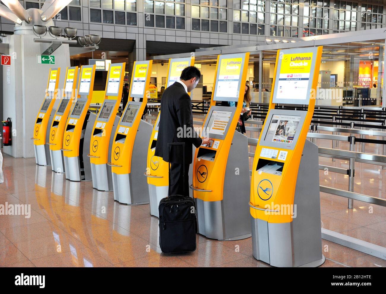 Terminali di check-in automatizzati da Lufthansa e un giovane uomo d'affari, sicuro di sé, che indossa un abito e un bagaglio per un viaggio d'affari all'Aeroporto di Amburgo, Amburgo, Germania, Europa Foto Stock