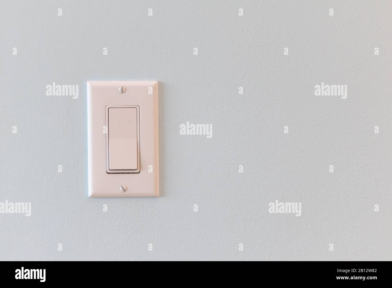 Un interruttore luminoso con un design a bilanciere a pannello piatto si trova su una parete di una casa. Foto Stock