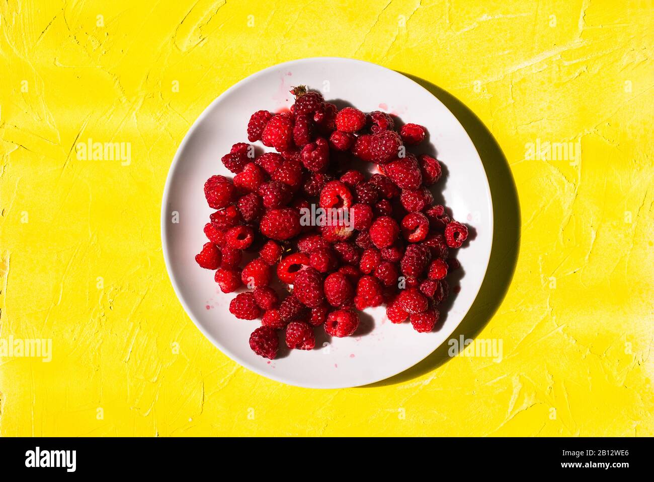 Piatto bianco con lamponi su fondo giallo con texture. Bacche rosse fresche con vitamine Foto Stock