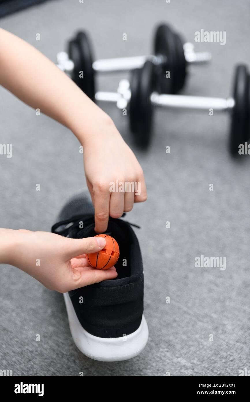 Mano circa per cadere una sfera di deodorante della scarpa nella scarpa di addestramento con i dumbells nello sfondo. Concetto per evitare l'odore sgradevole dopo l'attività. Foto Stock