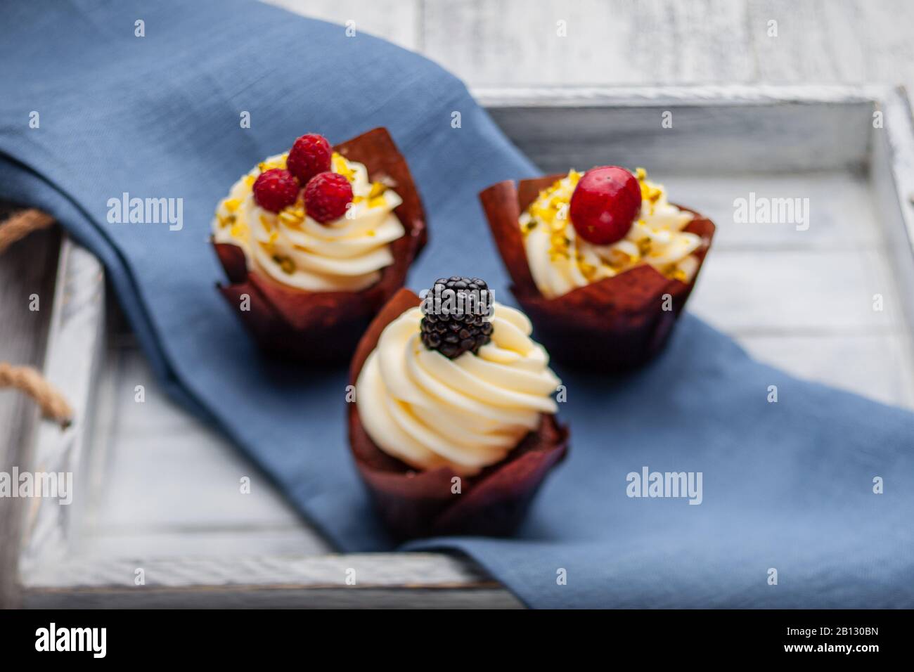 Muffin con cioccolato belga e crema di cioccolato bianco e mascarpone con frutti di bosco su un vassoio di legno Foto Stock