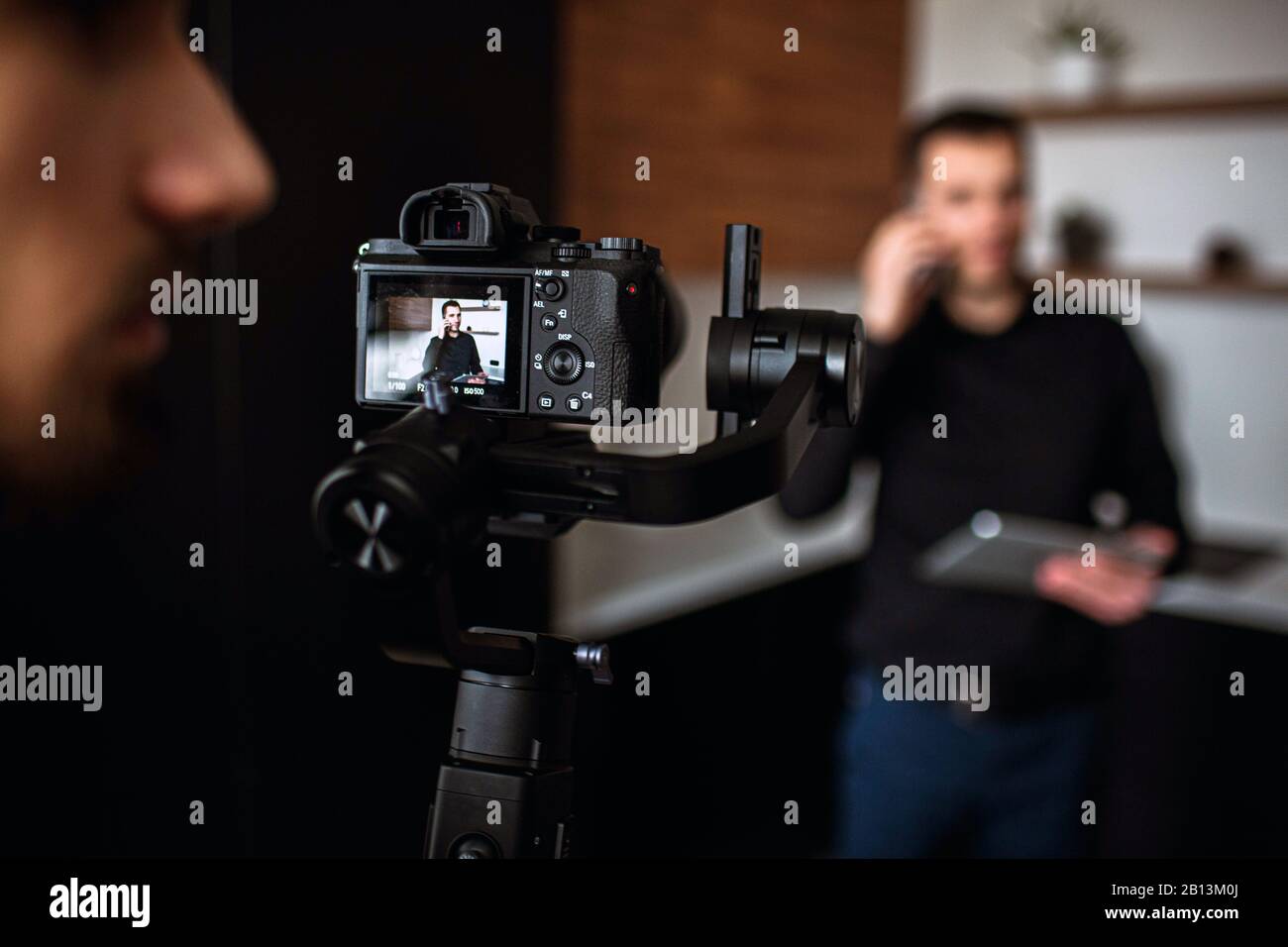 Immagine con sfondo sfocato dove il giovane uomo d'affari si trova in cucina e parla al telefono. Registrazione video di dusiness lavoro chiamata o riunione. Telecamera m Foto Stock