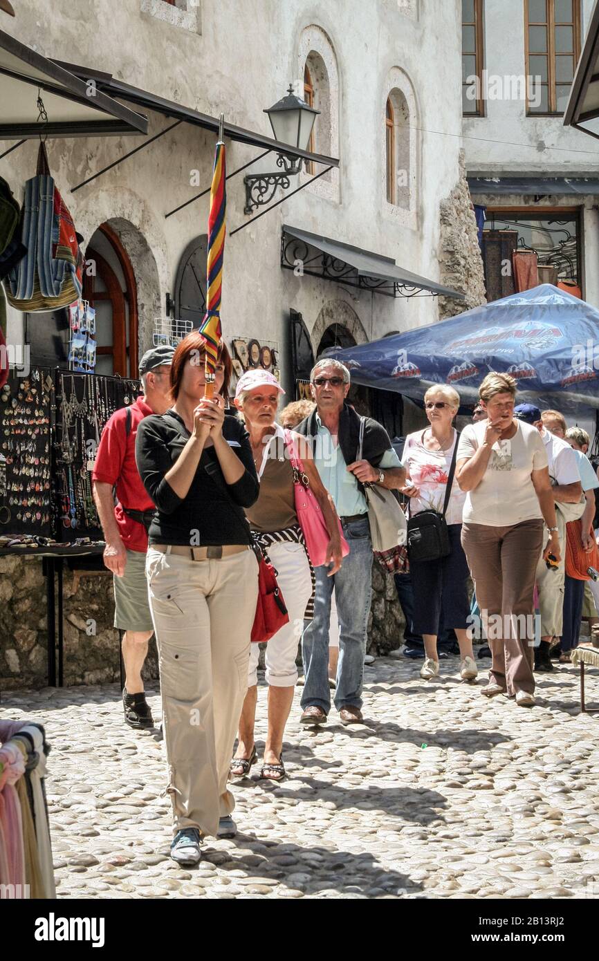 Mostar, BOSNIA - 6 GIUGNO 2008: Guida turistica femminile che tiene una pole per indicare la direzione da seguire ad un gruppo di turisti anziani nella città vecchia o Foto Stock