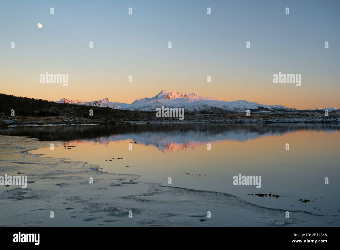 Le montagne in ultima luce della sera sono riflesse in un lago mentre la luna è nel cielo, Lofoten, Nordland, Norvegia Foto Stock