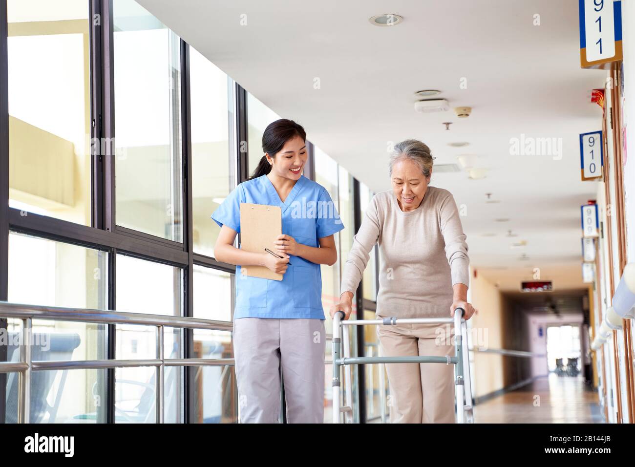 giovane fisioterapista asiatica che lavora con la donna anziana a camminare con un camminatore Foto Stock