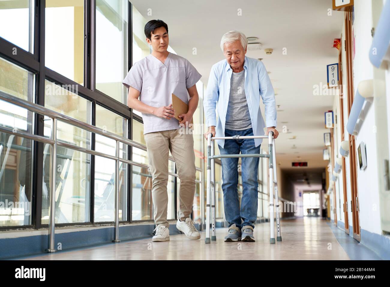 giovane fisioterapista asiatica che lavora con l'uomo anziano a camminare usando un camminatore Foto Stock