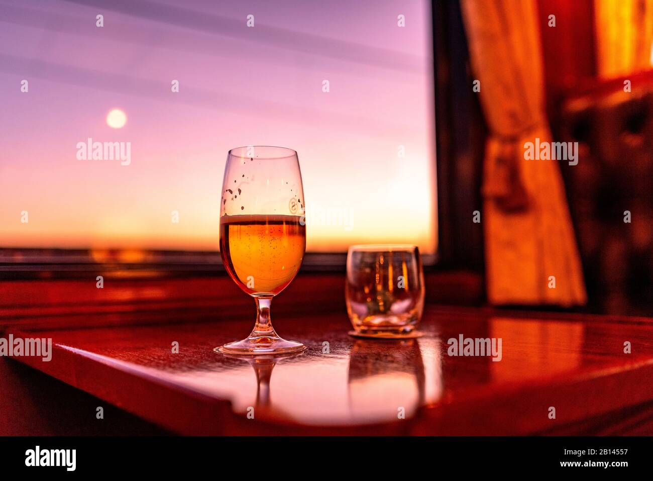 Un bicchiere di birra nel vano dei treni al tramonto Foto Stock