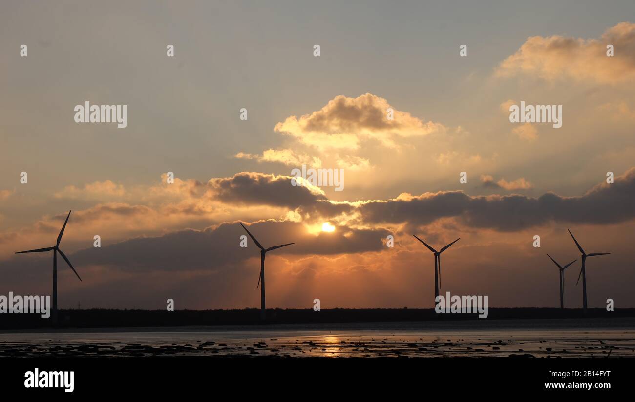 Turbine eoliche nella zona costiera, con tramonto del sole e un cielo nuvoloso sera. Foto Stock