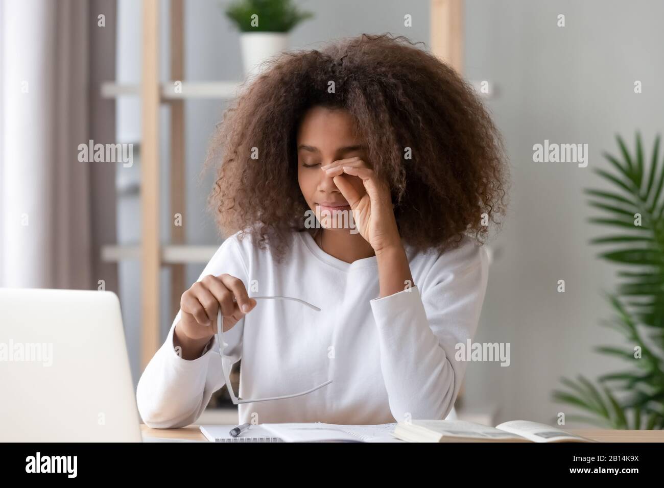 Ragazza africana teen che sfrega gli occhi stanchi dal calcolatore che tiene gli occhiali Foto Stock