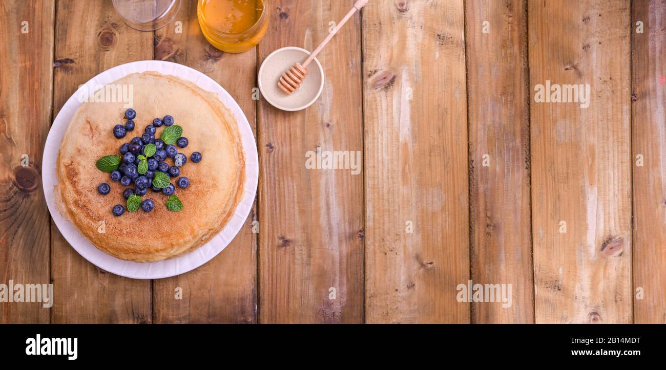Frittelle con mirtilli e miele su un piatto, su copertura in legno. Dolci tradizionali per il festival russo di Maslenitsa. Spazio libero per il testo. Foto Stock