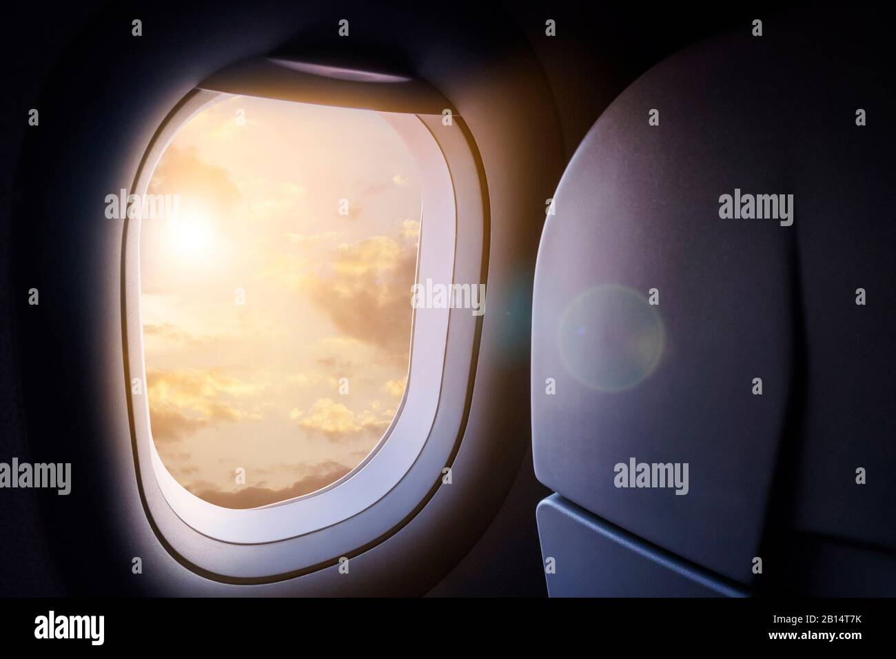 Nuvole e cielo con luce solare dorata e riflessi lenti come si vede attraverso la finestra di un aereo Foto Stock