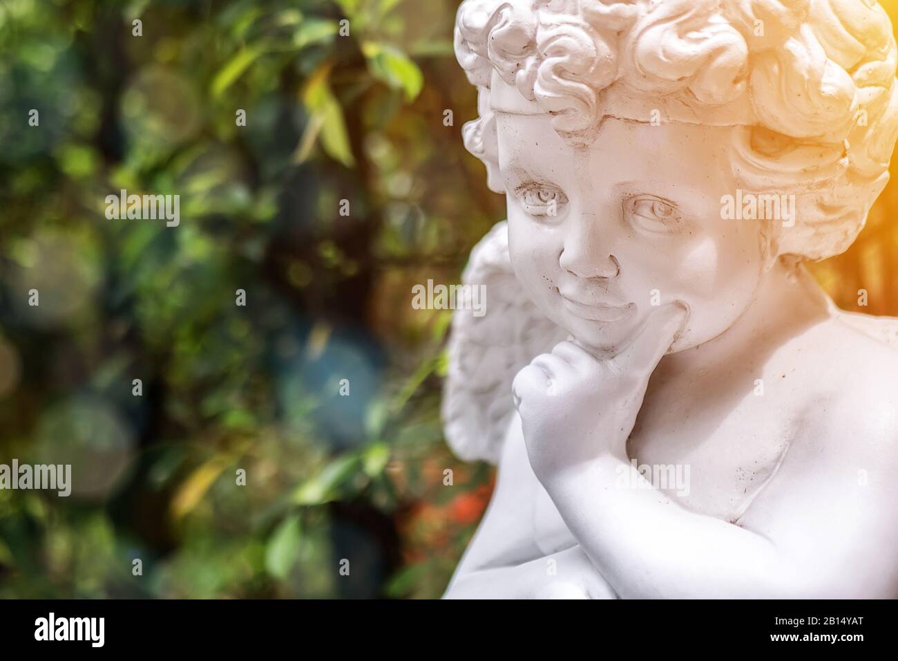 Il giardino decora il concetto dello sfondo. Bianco vintage statua Cupido in giardino con spazio copia verde sul lato sinistro. Luce mattutina , bockeh e fl. Lente Foto Stock