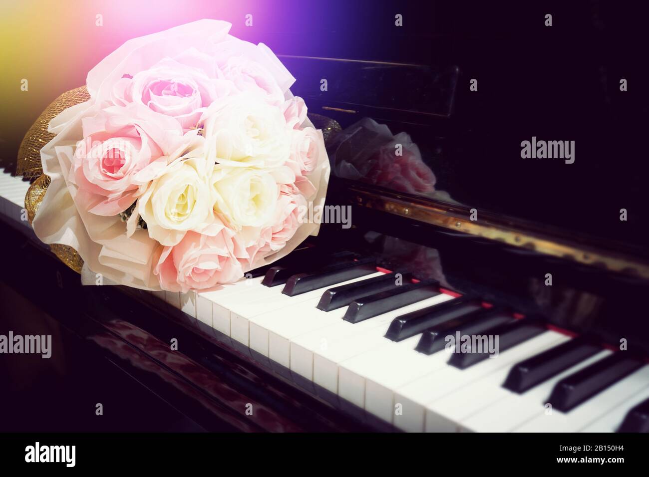Fiore di rosa al bouquet sulla tastiera del pianoforte con lieve bagliore in concerto. Immagine con messa a fuoco selettiva. Sfondo musicale con tonalità di colore calde Foto Stock