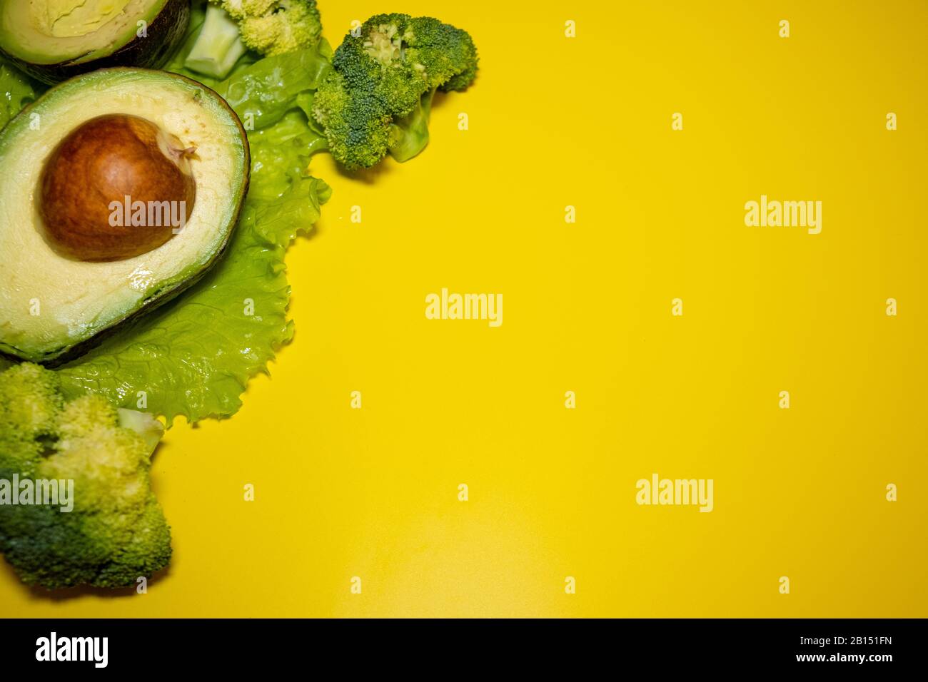 Avocado, lattuga verde, broccoli su sfondo giallo brillante. Concetto di alimentazione sana. Vista dall'alto. Spazio di copia Foto Stock
