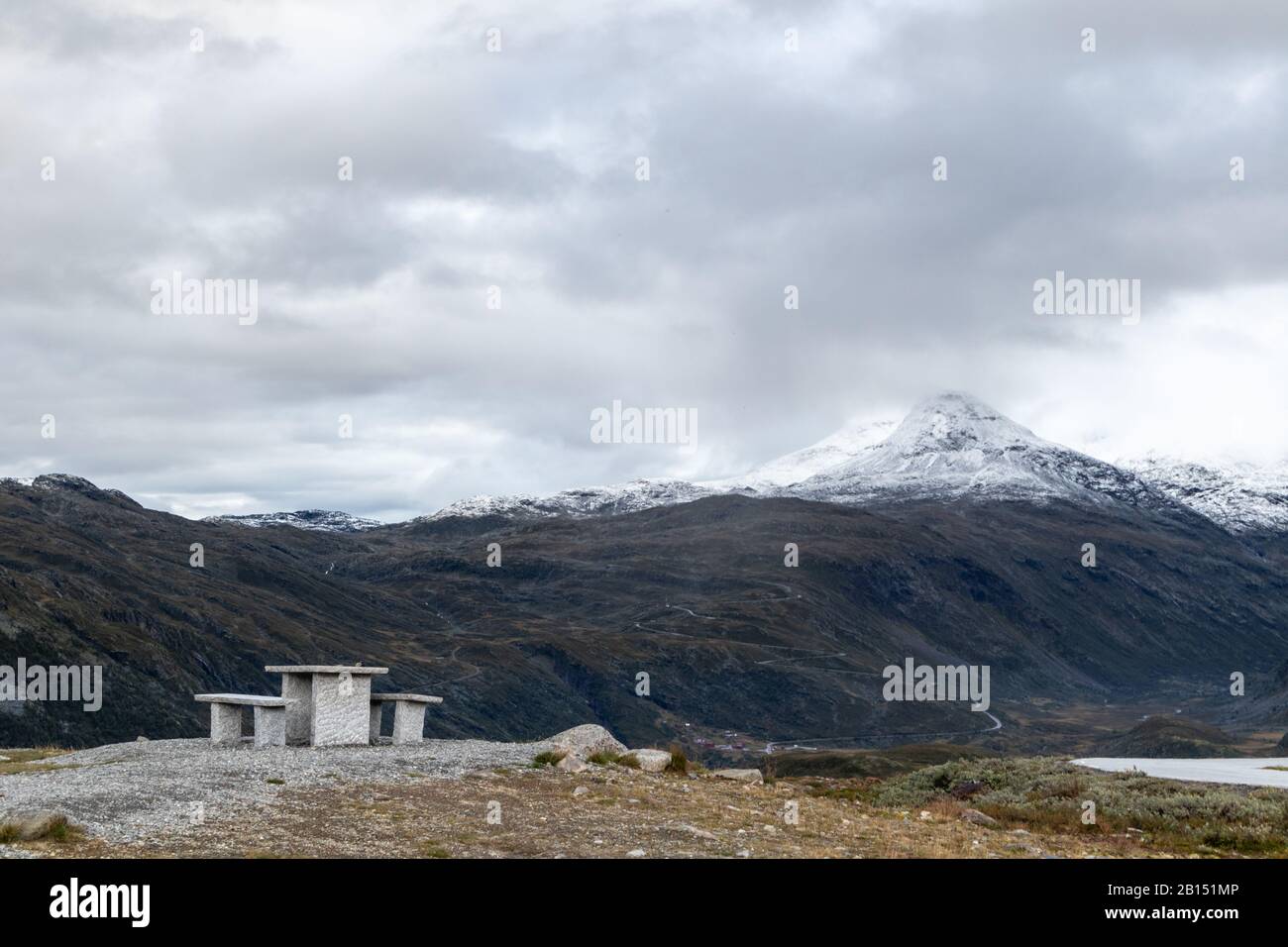 Montagna granito zona riposo panca vista con cime bianche neve e rocce, alte cime Norvegia paesaggio viaggio Norvegia, epiche nuvole in Tindevegen Foto Stock