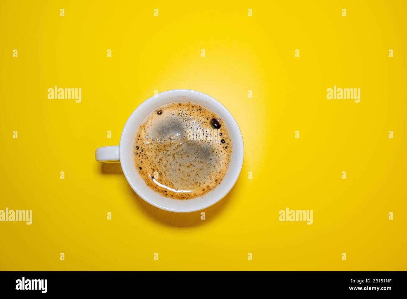 Tazza da caffè bianca con schiuma su sfondo giallo brillante vista dall'alto, concetto di minimalismo Foto Stock