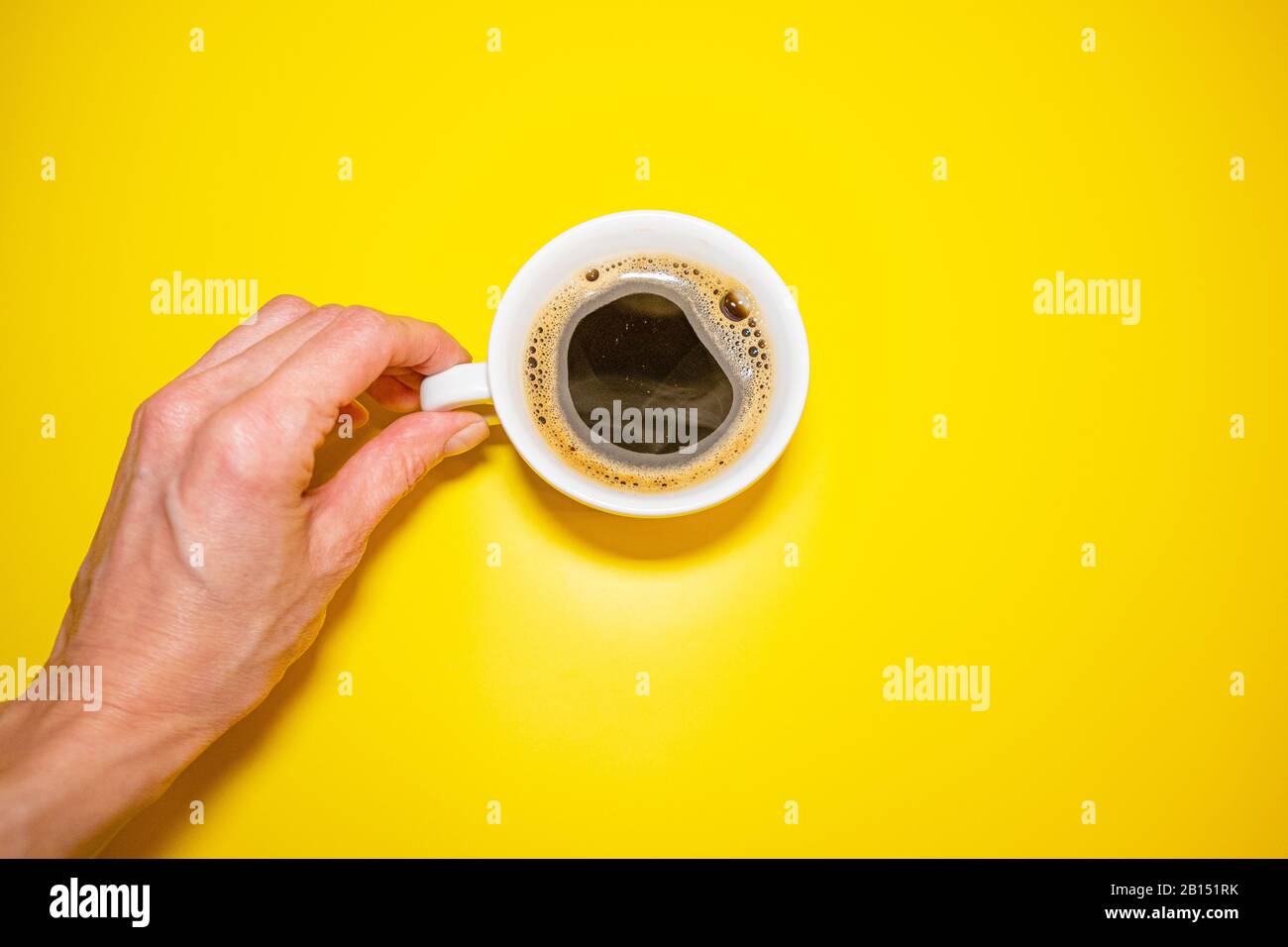 Mano femmina che tiene una tazza di caffè bianca su una vista dall'alto di sfondo giallo Foto Stock