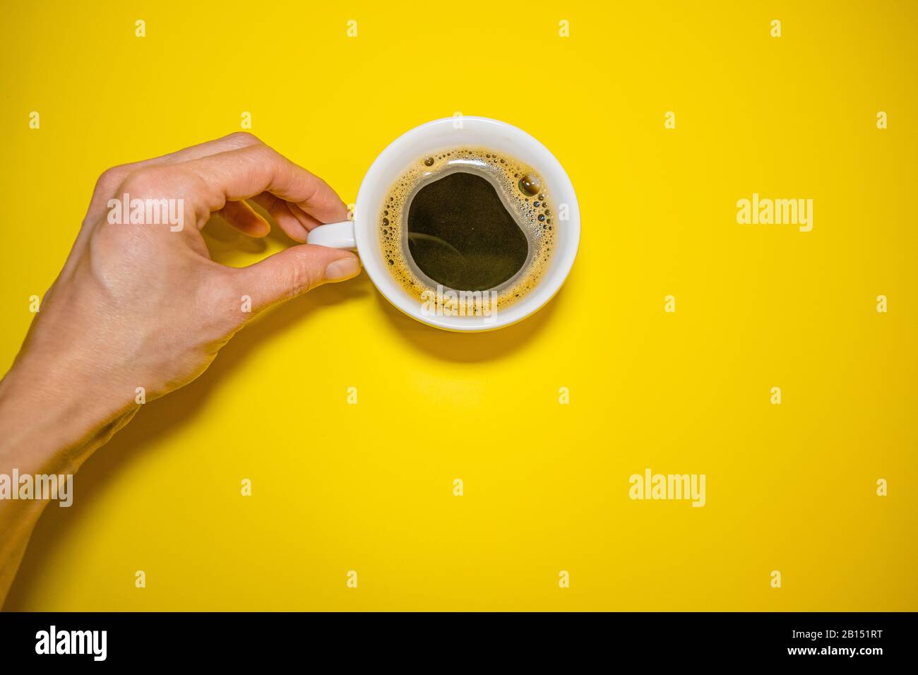 Mano femmina che tiene una tazza di caffè bianca su una vista dall'alto di sfondo giallo Foto Stock