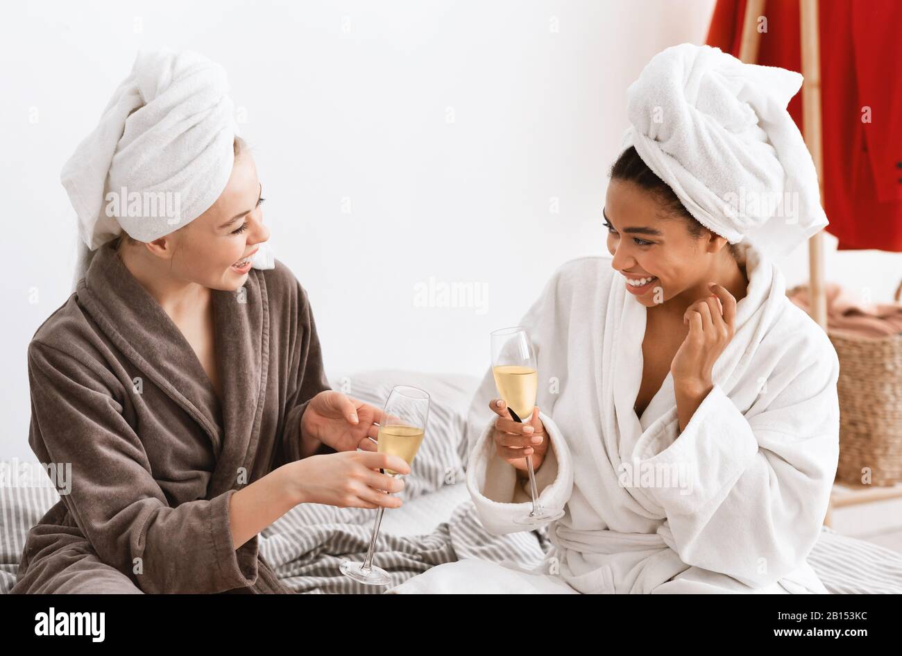 Le amiche multirazziali negli accappatoi celebrano il fine settimana, bevendo champagne Foto Stock