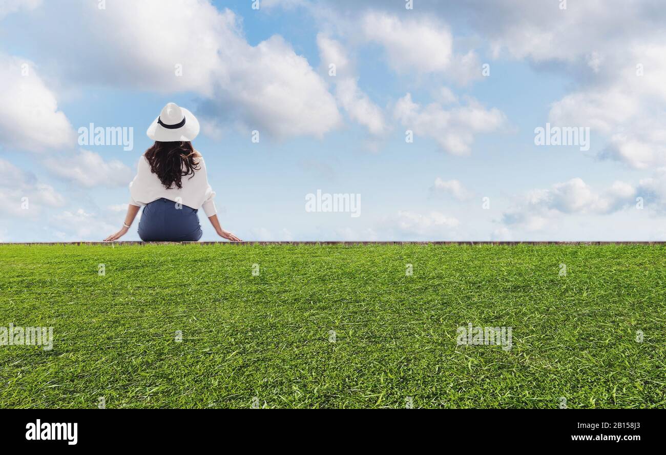 Donna seduta da sola su erba verde sotto cielo blu e nuvole bianche in estate Foto Stock