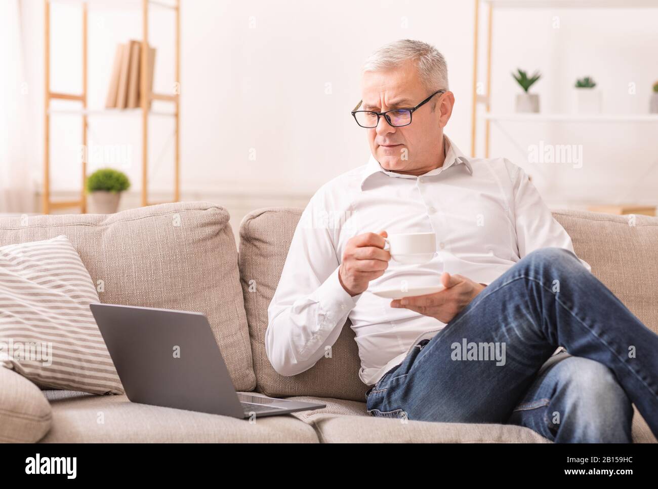 Uomo Anziano Che Guarda Il Laptop E Ha Tè Foto Stock